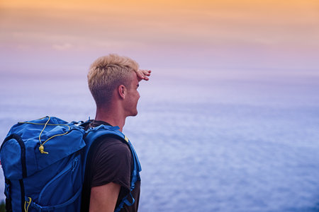Young man traveler and explorer is hiking the hill. Overlooking sea, ocean and hills on the horizon