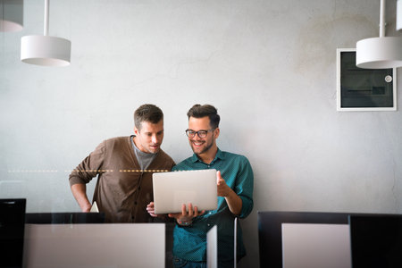 Young manager talking with experienced colleague while using computer in office.の写真素材