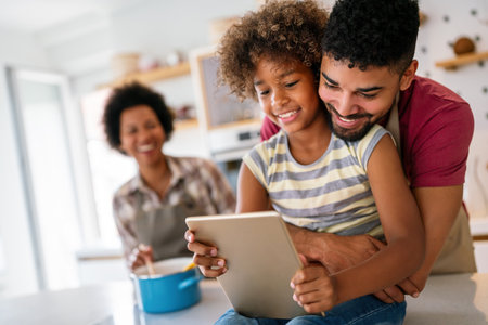 Happy african family having fun with device at home, using digital tablet looking at screen togetherの写真素材