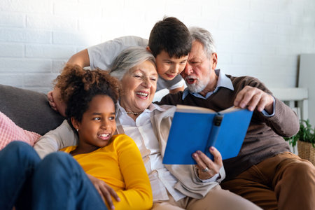 Happy senior grandparents having fun, reading book to multiethnic grandchildren.