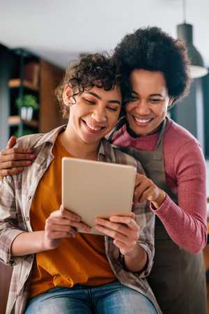 Happy african american mother helps teenage daughter with homework using digital tabletの写真素材