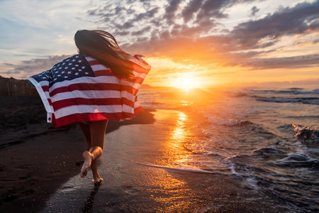 Happy woman holding american USA flag and running on the beach. Independence Day, travel conceptの写真素材