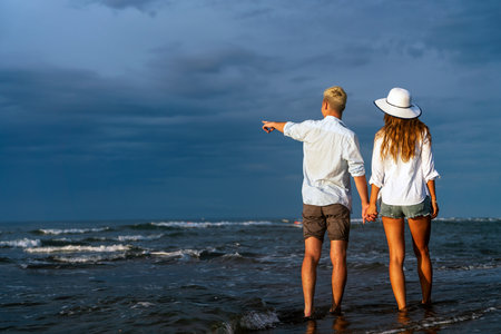 Young happy interracial couple walking on beach smiling, enjoying summer vacation, honeymoonの写真素材