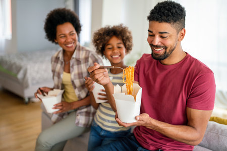 Happy african family eating at living room and enjoying time together. Home delivary takeaway foodの写真素材
