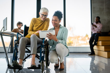 Disabled woman in wheelchair looking at computer, discussing startup project with interracial teamの写真素材