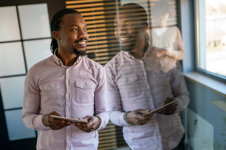 Relaxed smiling african american man holding digital tablet computer using appsの写真素材