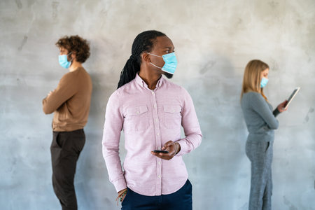 People in business style and medical masks standing with gadgets and keeping social distance.の写真素材