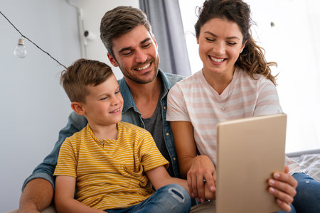 Happy family with kid having fun using tablet together, parents and child laughing relaxing at homeの写真素材