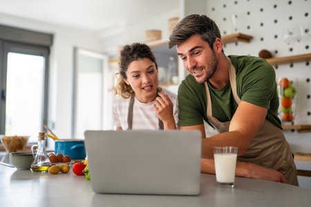Young couple using laptop computer to take part in online culinary workshop, cooking togetherの写真素材