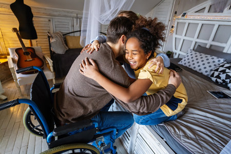 Multiethnic, diverse daughters and single father in a wheelchair sharing a warm moment at homeの写真素材