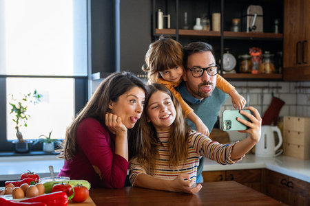 Happy parents with two kids using smartphone at home together, taking selfie, having fun togetherの写真素材