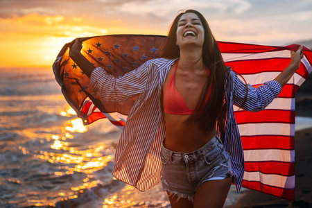 Happy woman smiling and running on beach with the US flag. July 4th independence day. Holidayの写真素材