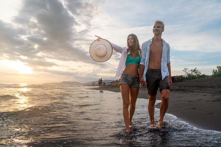 Young happy interracial couple walking on beach smiling, enjoying summer vacation, honeymoonの写真素材