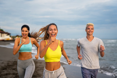 Group of young people, friends in sports clothing jogging while exercising on the beach outdoorsの写真素材