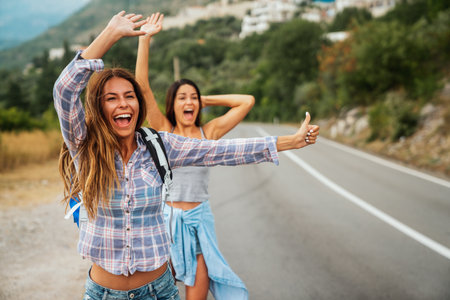 Cheerful interracial friends standing on road showing hitchhiking gestures. Tourism travelingの写真素材