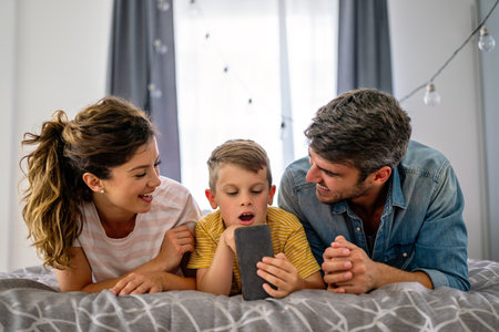 Happy parents with kid using smartphone at home together, playing, having fun with dogの写真素材