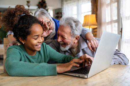 Smiling senior grandparents and cute black girl, granddaughter looking at laptop computer screenの写真素材