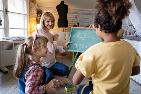 Smiling female teacher, mother showing new math task to elementary diverse schoolchildrenの写真素材
