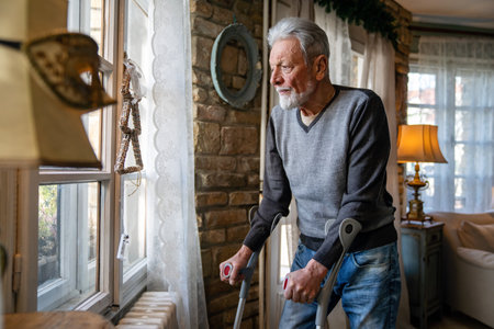 Old man with crutch feeling disappointed, lost in sad thoughts alone at home. Widow mature man.の写真素材