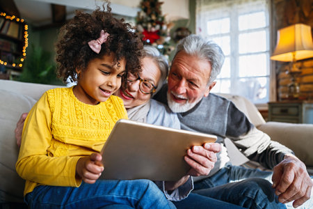 Mature couple with grandchild look at tablet screen and learn how to make video call or use laptopの写真素材