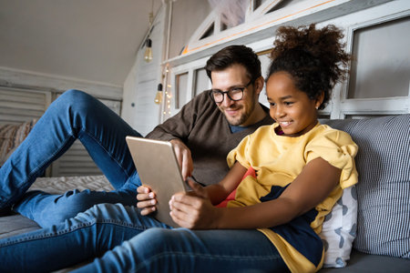 Single father playing with his multiethnic, diverse kid on the bed with digital tablet at homeの写真素材