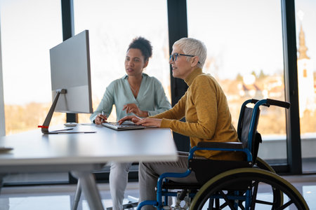 Disabled woman in wheelchair looking at computer, discussing startup project with interracial teamの写真素材