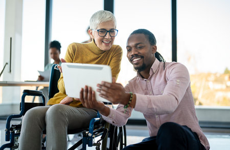 Business woman in wheelchair working with colleague in modern inclusive office. Diversity, supportの写真素材