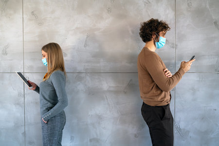 People in business style and medical masks standing with gadgets and keeping social distance.の写真素材