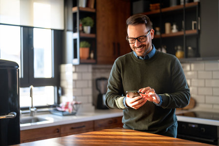 Checking his messages over coffee. Man using a smart phone while drinking coffee at homeの写真素材