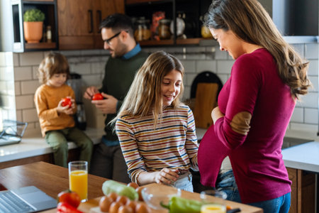 Pregnant mother, daughter tenderly embracing while father and son having fun at home during the dayの写真素材