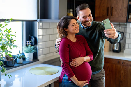 Man hugging his pregnant wife, having fun together making selfies in the last trimester of pregnancyの写真素材