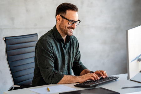 Young happy successful business man working with computer in corporate officeの写真素材
