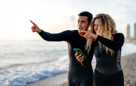 Young people, surfers walking on the coast while using mobile phone and enjoying summer vacationの写真素材