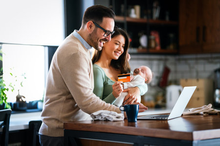 Cheerful young family with a baby child enjoying online purchasing on the internet at homeの写真素材