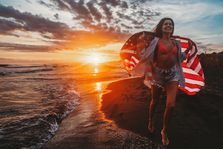 Young woman holding national American flag walking ocean beach. America Independence Day conceptの写真素材