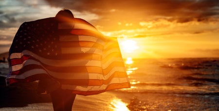 Young woman holding national American flag walking ocean beach. America Independence Day conceptの写真素材