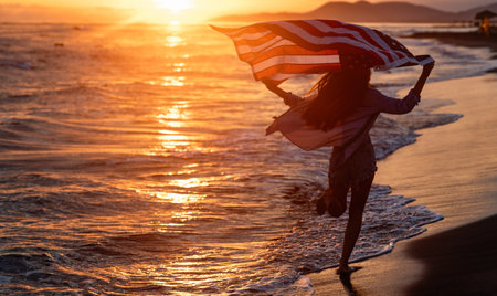 Happy woman holding american USA flag and running on the beach. Independence Day, travel conceptの写真素材