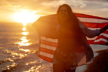 Young woman holding national American flag walking ocean beach. America Independence Day conceptの写真素材