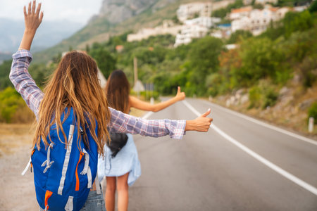 Cheerful interracial friends standing on road showing hitchhiking gestures. Tourism travelingの写真素材