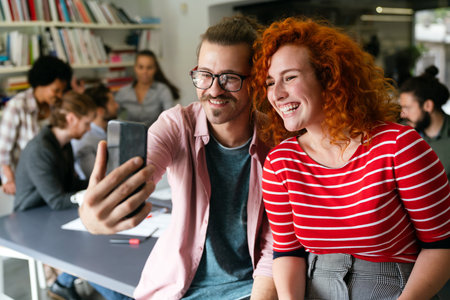 Friendly happy multiethnic coworker male and female having fun with smartphone, working togetherの写真素材