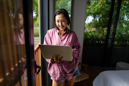 Middle eastern, asian woman working on a laptop in a tropical-inspired home officeの写真素材