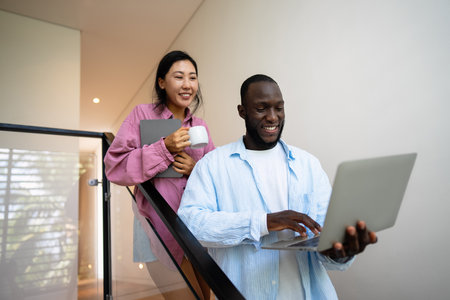 Young happy multiethnic couple having fun while using laptop, digital device at homeの写真素材