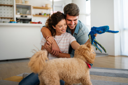 Happy couple playing with dog, having fun on floor at home. Married couple with cute petの写真素材