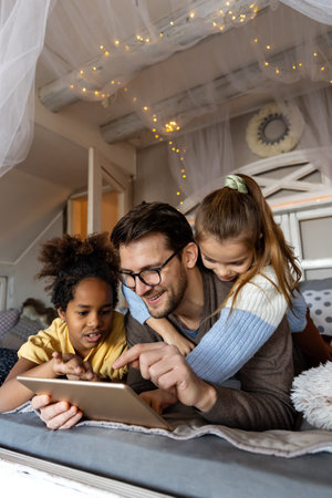 Single father playing with his multiethnic, diverse kids on the bed with digital tablet at homeの写真素材