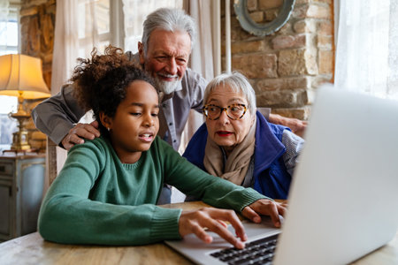 Joyful multiethnic grandparents with grandchild watching online game on laptop at home togetherの写真素材