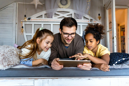 Happy diverse family resting at home on bed spending time together and using digital gadgets.の写真素材