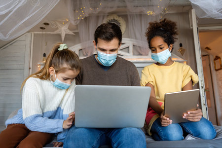 Diverse father working on a laptop while daughter is reminding him that she has online meetingの写真素材