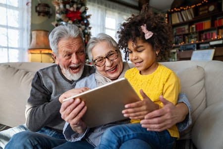 Mature couple with grandchild look at tablet screen and learn how to make video call or use laptopの写真素材