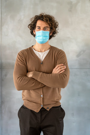Young man with curly hair putting on his face mask to protect himself from illness, gray backgroundの写真素材