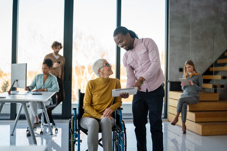 The image includes a person using a wheelchair, depicting inclusivity and teamwork in modern officeの写真素材